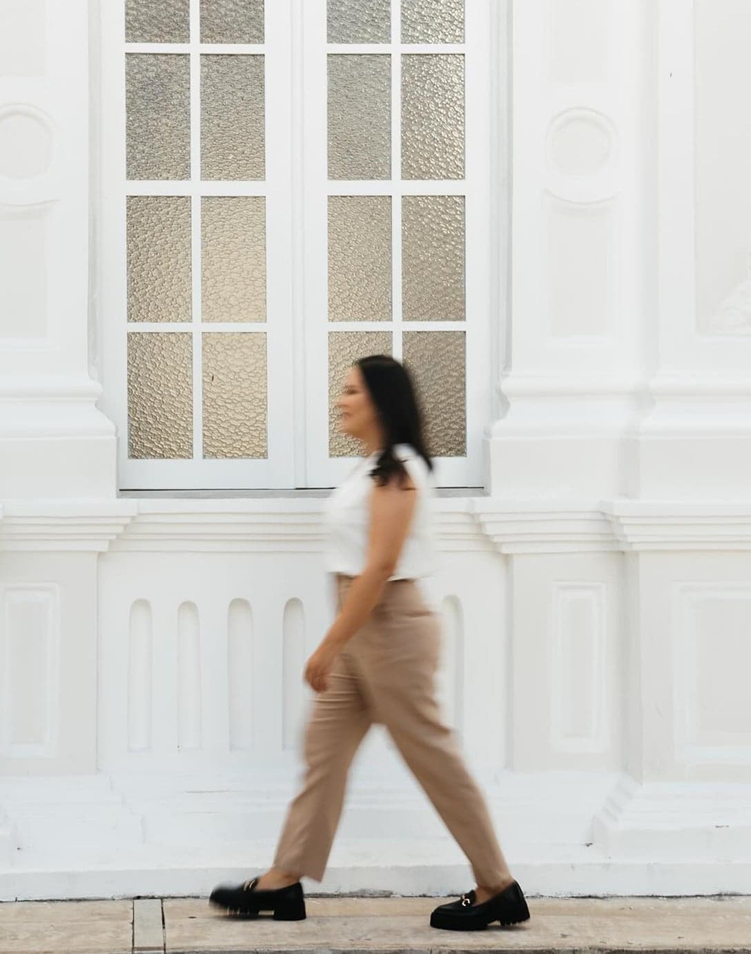 Mulher caminhando em frente a uma fachada branca com janela de vidro texturizado, imagem da rotina de quem vive nos projetos da TRUÍV